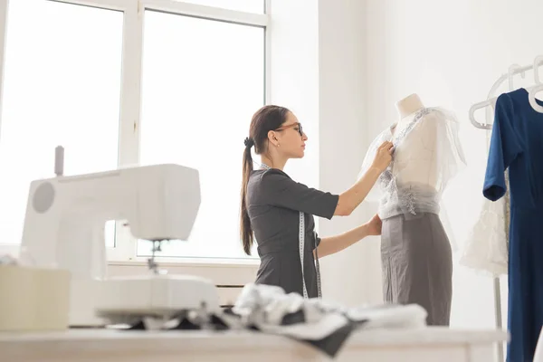 Dressmaker, tailor, fashion and showroom concept - Side view of female fashion designer measuring materials on mannequin in office