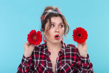 Elinde farklı kalpler ile kırmızı çiçekler tutan güzel bir genç sürpriz kadın yakın çekim portre mavi bir arka plan üzerinde poz. Farklılıklar ve hassas nüanslar kavramı.