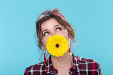 Retro görüntü komik pozitif genç kadın mavi bir arka plan karşı poz dişlerinde parlak sarı gerbera çiçek tutan. Sürpriz ve eğlence kavramı.