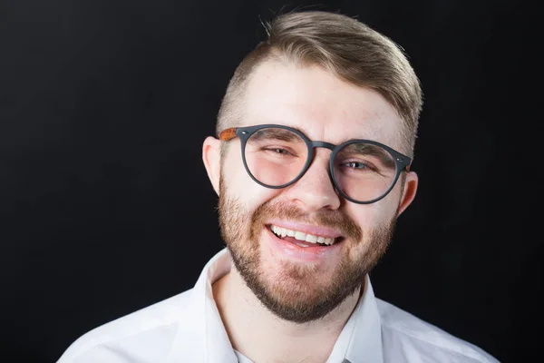 Close up retrato de homem barbudo bonito rindo em óculos elegantes de pé contra a parede preta — Fotografia de Stock