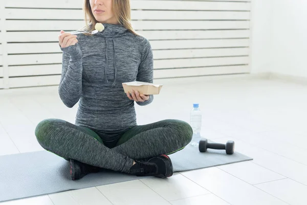 Sport, healthy lifestyle and people concept - young woman with healthy food and a dumbbell sitting on the floor