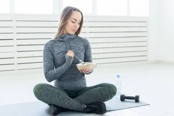 Deporte, estilo de vida saludable y concepto de personas: mujer joven con comida saludable y una mancuerna sentada en el suelo — Foto de Stock