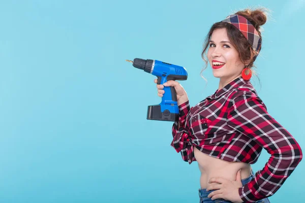 Δροσερό θετική νεαρή γυναίκα σε ένα καρό πουκάμισο κρατώντας ένα κατσαβίδι που ποζάρει σε μπλε φόντο με χώρο αντιγραφής. Έννοια της επισκευής και της κατασκευής. — Φωτογραφία Αρχείου