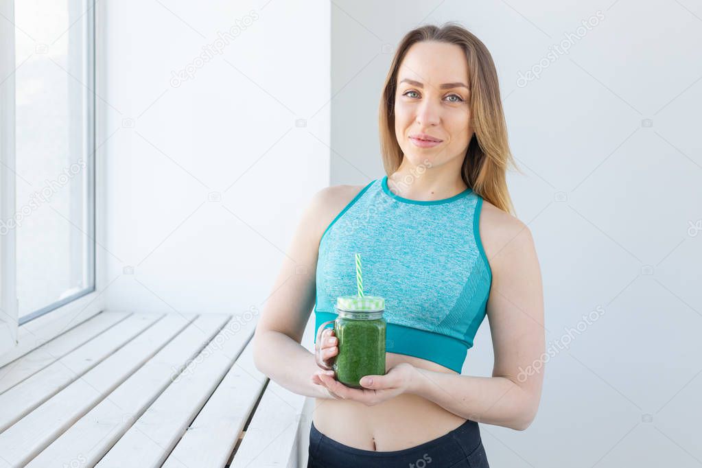 Healthy, diet, detox and weight loss concept - young woman in sportswear with green smoothie