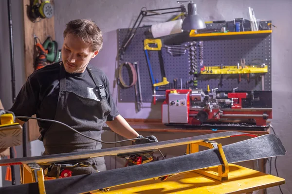 Un uomo in abiti da lavoro riparatore in officina servizio sci riparazione dello sci — Foto Stock