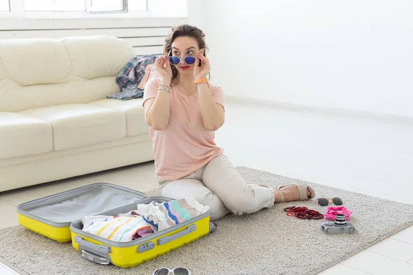 Tatil, yolculuk ve seyahat konsepti - Genç Kadın yatak odasında evde bir bavul toplar, bir çok şey, tatil ve sarı bavul — Stok fotoğraf