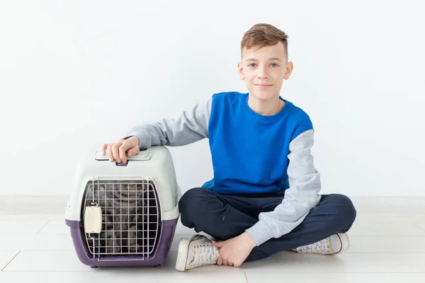 Riéndose niño positivo sostiene una jaula con un gato pliegue escocés al lado de él sentado en el suelo en un nuevo apartamento. Concepto de protección animal . — Foto de Stock