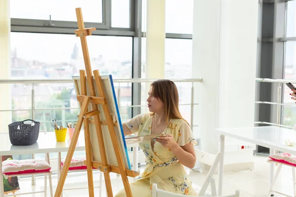 Lezione d'arte, disegno e creatività - Studentessa seduta davanti al cavalletto con tavolozza e pennello — Foto Stock