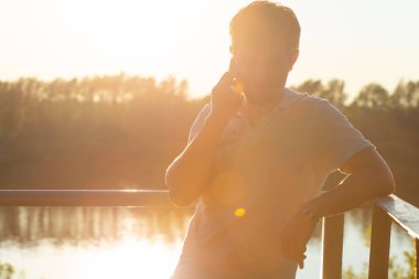 Doğa, teknolojiler ve iletişim konsepti - Yakışıklı adam açık havada akıllı telefon kullanarak.