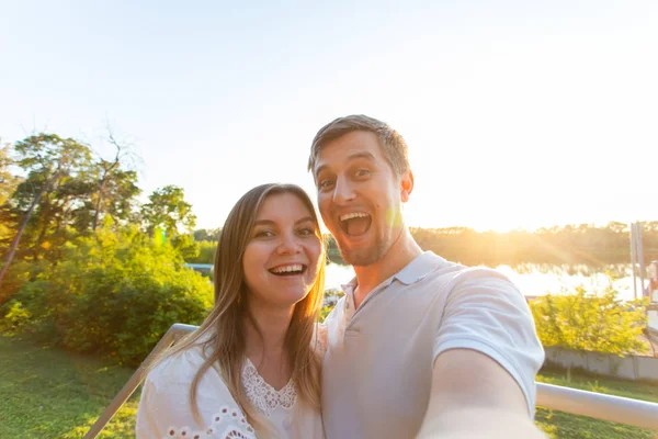 Casal romântico engraçado bonito no fundo da natureza. Jovem atraente e homem bonito estão fazendo selfie, sorrindo e olhando para a câmera . — Fotografia de Stock