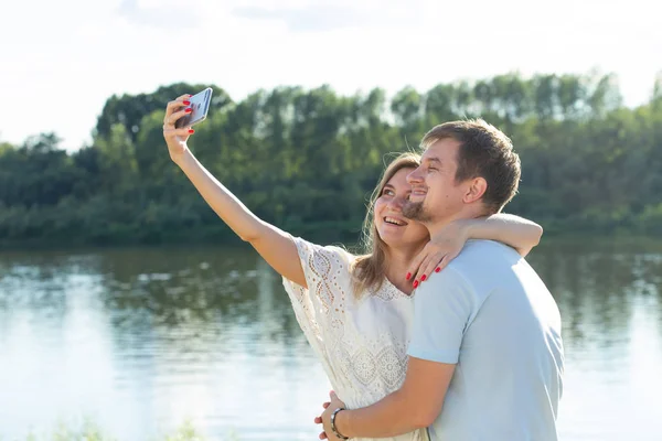 Capturar momentos brilhantes. Joyful jovem casal amoroso fazendo selfie na câmera enquanto está de pé ao ar livre — Fotografia de Stock