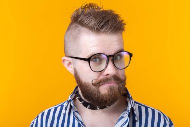 Sarı bir arka planda poz gömlek bıyık sakal ve fetiş kolye ile genç pozitif trendy adam hipster. Rock ve alt kültür konsepti.