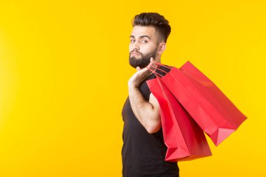 Adam sarı bir arka planda kırmızı alışveriş torbaları tutuyor. Süpermarket ve hediyeler alışveriş kavramı. Reklam alanı.