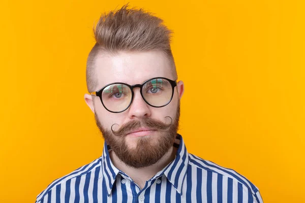 Joven hombre de moda positivo hipster con una barba bigote y collar fetiche en camisa posando sobre un fondo amarillo. Concepto de roca y subcultura . — Foto de Stock