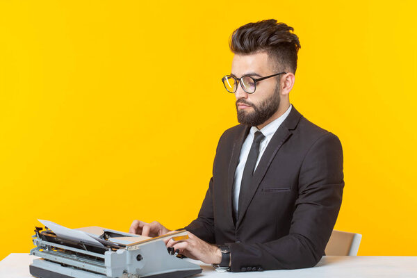 Арабский бизнесмен или менеджер в формальном костюме печатает текст на пишущей машинке на жёлтом фоне. Концепция деловой и офисной работы
