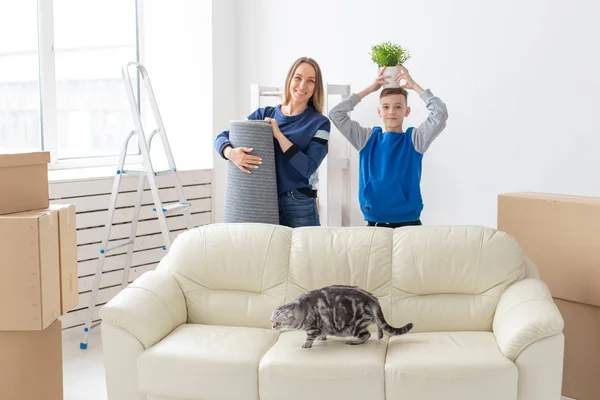 Die junge, süße alleinerziehende Mutter und ihr Sohn freuen sich über den Umzug in ihr neues Haus, in der Hand halten sie eine schottische Raubkatze und einen Topf mit Grünzeug. Konzept der Wohnungserwärmung und der Erweiterung des Familienraums. — Stockfoto