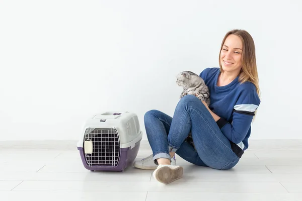 Encantadora joven positiva sostiene en sus manos a su hermoso gato escocés gris plegado sentado en el suelo en un nuevo apartamento. Concepto de mascota . — Foto de Stock