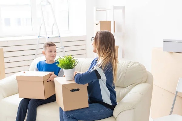 Nette alleinerziehende Mutter und kleiner Sohn sortieren nach dem Umzug Kisten mit Sachen. das Konzept der Eigenheimhypothek und die Freude am neuen Wohnraum. — Stockfoto