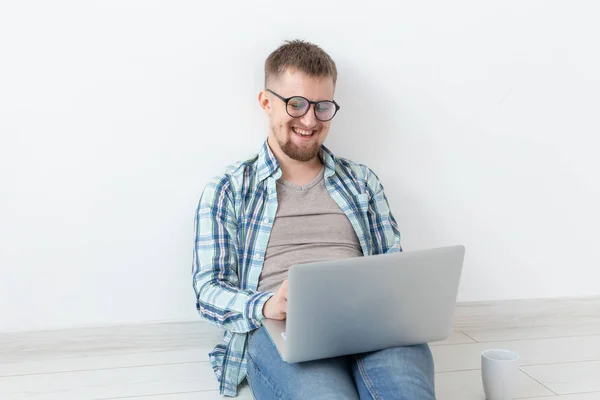 Pozytywny młody człowiek w casual ubrania i okulary surfowania po Internecie za pomocą Wi-Fi i laptopa w poszukiwaniu mieszkań wynajmu. Koncepcja houseocieplenia i wyszukiwania mieszkania. — Zdjęcie stockowe