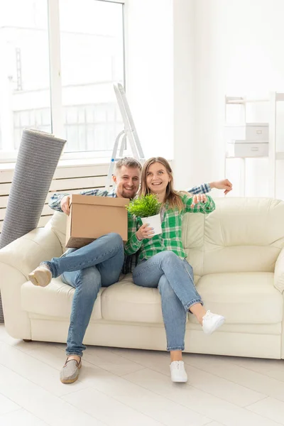 Позитивная веселая пара радуется переезду своей новой квартиры, сидя в гостиной с вещами. Концепция новоселья и ипотеки для молодой семьи . — стоковое фото