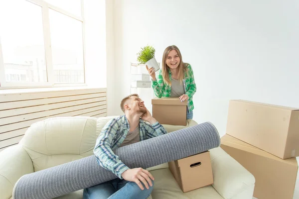 Satisfeito jovem casal alegre homem forte e mulher bonita segurando suas coisas em suas mãos sentado na sala de estar de um novo apartamento. Conceito de aquecimento doméstico . — Fotografia de Stock