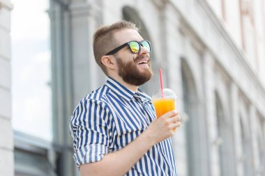 Şık bir bıyık ve elinde meyve suyu ile bir sakal ile oldukça neşeli genç işadamı yan görünümü, bir iş gününden sonra şehir etrafında yürüyüş. Pozitif ve dinlenme kavramı.