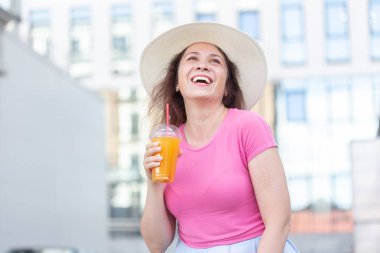 Sıcak bir yaz gününde suyu ile şehirde dolaşan bir şapka genç güzel neşeli kadının alt görünümü portre. Hafta sonu şehirde yürüme kavramı.