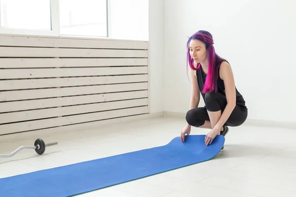 Niña delgada hipster con el pelo de color yacía una alfombra de gimnasia en el suelo En el gimnasio brillante antes del comienzo del entrenamiento. Concepto de un cuerpo delgado y saludable y estilo de vida deportivo . — Foto de Stock