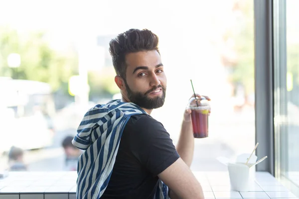 Positivo joven elegante chico beber jugo en un café durante un descanso en el trabajo. El concepto de descanso y merienda saludable . — Foto de Stock