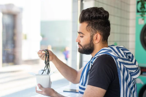 Positieve jonge stijlvolle kerel die Chinese noedels eet in een café tijdens een pauze op het werk. Het concept van rust en gezonde snack. — Stockfoto