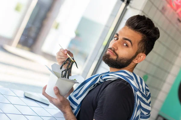 Positivo joven elegante chico comiendo fideos chinos en un café durante un descanso en el trabajo. El concepto de descanso y merienda saludable . — Foto de Stock