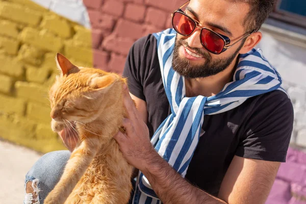 애완 동물 소유자와 우정 개념 - 잘 생긴 아랍 남자는 귀여운 생강 고양이를 잡고 포옹하고 있습니다. 호기심이 많은 표정을 가진 고양이 클로즈업 — 스톡 사진