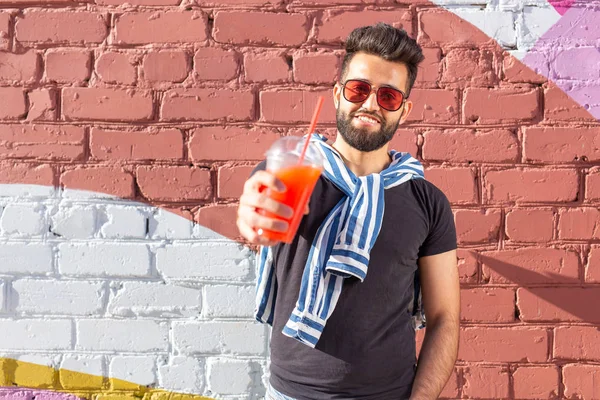 Schattig stijlvolle Arabische jonge mannelijke hipster met een snor en een baard en het dragen van glazen drinken sap met een rietje. Zomer vakantie concept. — Stockfoto