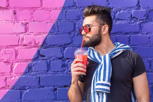 Retrato de un joven árabe alegre positivo con un vaso de jugo con una pajita mientras camina por la ciudad en un cálido día soleado de verano. El concepto de descanso después del estudio y el trabajo los fines de semana . — Foto de Stock