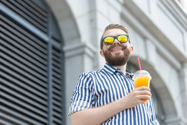 Portret van een wazig stijlvolle jonge hipster man met baard en snor houden van verse sinaasappelsap in zijn handen. Gezond snack concept. — Stockfoto