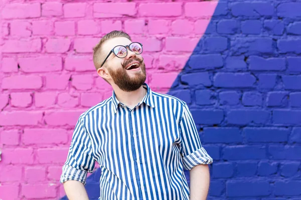 Retrato é um bom jovem com um bigode e uma barba posando contra uma parede de tijolo azul-violeta . — Fotografia de Stock