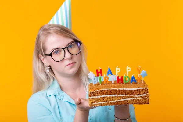 有趣的积极年轻女子在她的手中拿着一个自制的蛋糕与题词生日快乐，在黄色的背景。假日和纪念日的概念. — 图库照片
