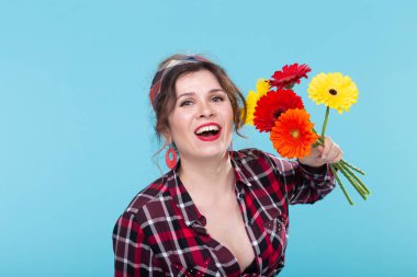 Ekose gömlek ve mavi bir arka plan üzerinde poz güzel parlak gerbera çiçekler koklama bir bandaj güzel pozitif genç kadın. Hediye ve selam kavramı.