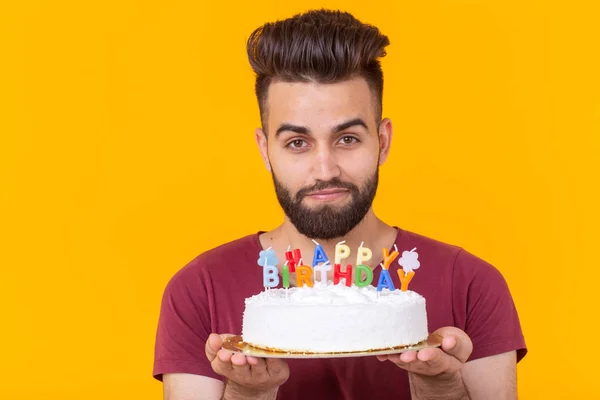 Young male hipster with a beard holding a cake with the inscription happy birthday congratulations on the anniversary and the holiday. Concept of promotions and discounts.