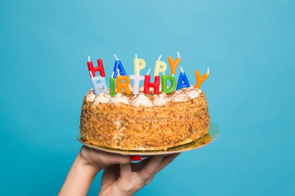 Manos sosteniendo un pastel de cumpleaños con velas y el cumpleaños de la inscripción sobre un fondo azul. Copiar espacio —  Fotos de Stock