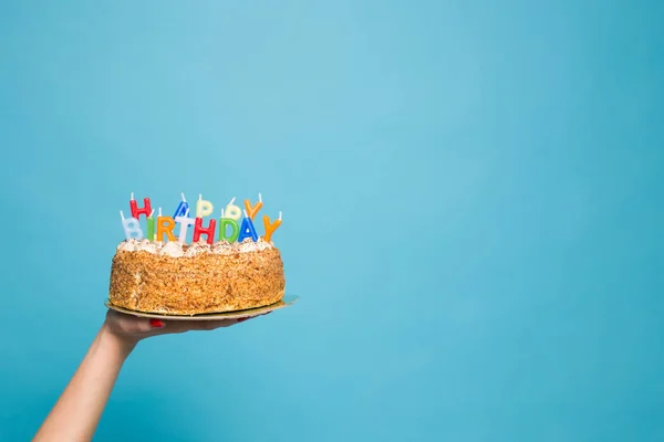 Manos sosteniendo un pastel de cumpleaños con velas y el cumpleaños de la inscripción sobre un fondo azul. Copiar espacio —  Fotos de Stock