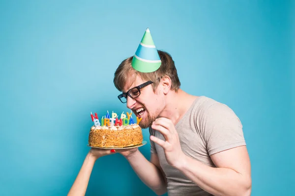 Vicces őrült fiatalember egy üdvözlőpapír kalap akar harapni le egy darab gratuláló torta. Fogalma bolondozás körül, és születésnapi üdvözletet. Lemezterület másolása — Stock Fotó