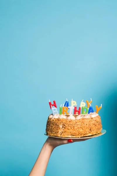 Hands holding a birthday cake with candles and the inscription birthday on a blue background. Copy Space