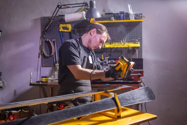 Muž v opraváři pracovních oděvů v dílně, opravování lyžařských — Stock fotografie