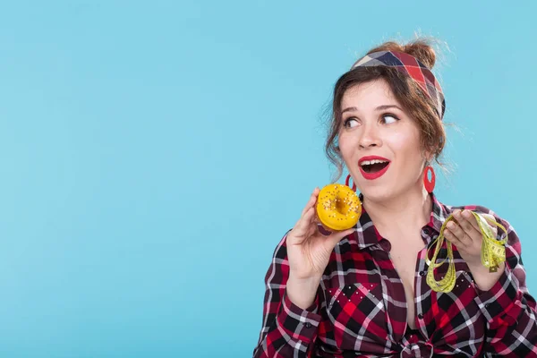 Close-up shocked surprised young beautiful woman looking at measuring tape and holding a green donut in hands posing on a blue background with copyspace. Concept of diet and rejection of harmful high