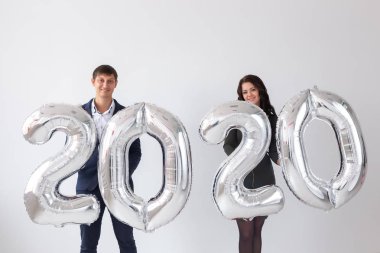 Yeni yıl, kutlama ve tatil konsepti - beyaz arka plan üzerinde yeni yıl için gümüş balonlardan yapılmış 2020 işareti ile eğlenen aşk çift