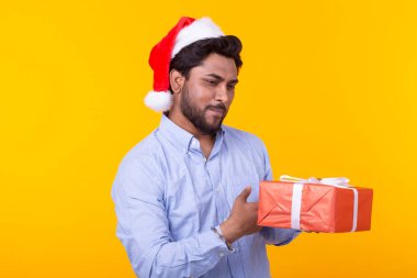 Hediyeler ve Noel ağacı sarı bir arka plan üzerinde poz ile Pozitif genç hint adam Noel Baba. Noel ve Yeni Yıl tatili konsepti.