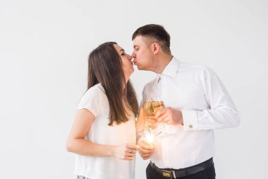 Yeni yıl, tatiller, tarih ve sevgililer günü konsepti - Beyaz arka plan üzerinde kıvılcımLar ışık ve şampanya bardak tutan Loving çift