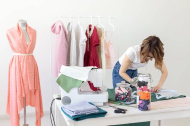 Pozitif genç güzel kız terzi tasarımcısı atölyesinde bir dikiş makinesi ile masasında otururken yeni bir proje üzerinde çalışıyor. Yaratıcı iş konsepti.