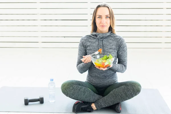 sport, healthy, people concept - Girl holding salad and dumbbell after fitness training